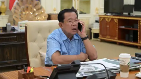 Hun Sen/ Facebook Hun Sen in a half-sleeved blue shirt at his desk, talking on the phone. 