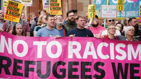 PA Media Counter protestors outside the Radisson Blu in Perth. They hold a banner which says "no to racism, refugees welcome" and signs which say things like "we stand with refugees" and "smash racism"