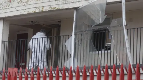 PACEMAKER A person in a forensic suit entering a flat. Red railings are at the bottom.