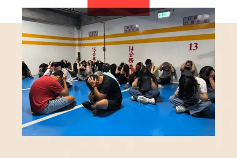 Tessa Wong/ BBC People in Kinmen with their hands over the heads sitting on the floor, as part of one of the drills