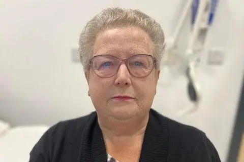 Margaret Junner, an older woman with short grey hair and glasses, wearing a dark coloured cardigan, looks at the camera.