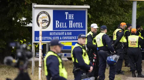 PA Media A group of police in hi-vis vests stand in front of a blue and white sign for The Bell Hotel in Epping.
