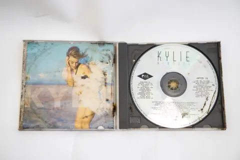 Great Ormond Street Hospital for Children The CD of Kylie Minogue's album Rhythm of Love is open on a table. There is rust and dirt on different areas of the CD, which is metallic silver in colour. 