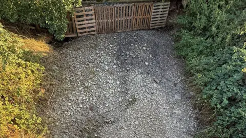 Dave Lister A brook is shown with the water levels completely depleted, with stones visible on what was once the brook bed. There are bushes on either side of it. A brown gate can be seen fencing off the brook.