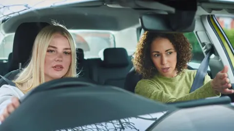 Getty Images A stock image of a blonde learner driver listening to guidance from an instructor