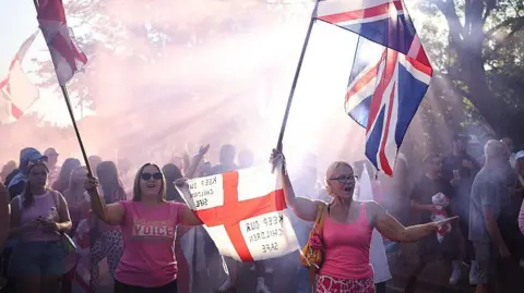 Getty Images A protest outside the Bell Hotel. Two women are holding St George and Union flags. On one flag is written the message: "Keep our children safe".