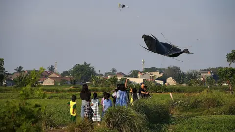 Haryo Bangun Wirawan/BBC Back view of a group of children and teens looking at the sky, as they fly kites in a field