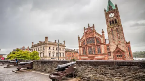 Getty Images In the foreground on the wall we have several cannons sticking out between the battlements. A girl accompanied by a boy takes pictures of another girl who has climbed a cannon on the wall To the right outside the wall is The Guildhall, building located next to the river, very close to the center of the city, built in 1887 of sandstone and brick. 