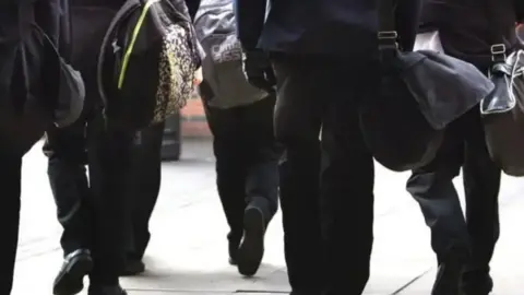 PA Media A stock image of the backs of pupils, from the shoulders down. They are wearing black school uniform and carrying bags