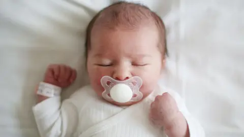 Getty Images A baby sleeping with a large white dummy in its mouth.
