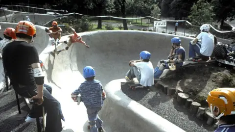Iain Urquhart Young people in 1978 wearing helmets and other safety gear skateboarding at Kelvin Wheelies skatepark