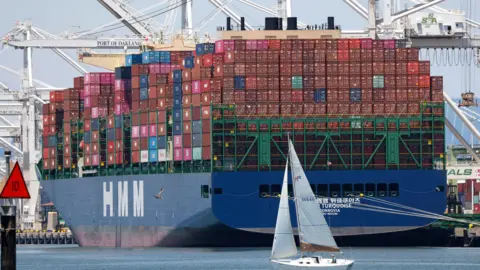 EPA A sailboat sails past a container ship at the Port of Oakland in Oakland, California