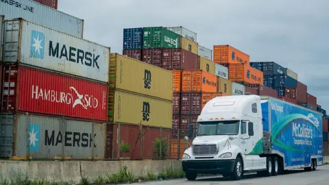 Bloomberg/Getty A blue and white McCollister's Transportation Group tractor trailer drives past a pile of shipping containers at the Port of Baltimore in Baltimore, Maryland, US, on Friday, Aug 1, 2025.