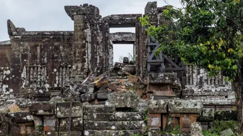 BBC/Jonathan Head Stone stairways leading up to an ancient temple appear damaged, with some parts of it having collapsed. A tree stands next to the entrance of the temple.