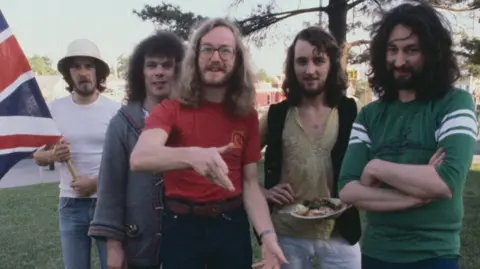 Getty Images The five members of Supertramp standing together outdoors in a row, with bassist Dougie Thomson holding a union flag