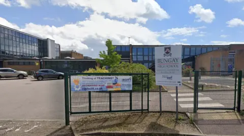 Google The exterior of Bungay High Sixth Form. There is a gate in front of the school which is partly open. Cars can be seen parked in the car park outside the school building.