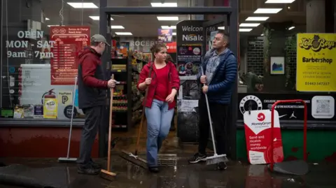Getty Images Staff with brooms clear water and mud from entrance to shop