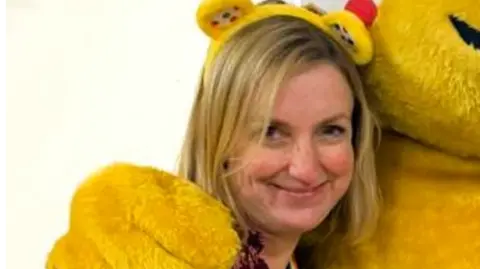 Louise Evans Louise wearing a floral burgundy top and yellow Pudsey head band smiling for the camera.