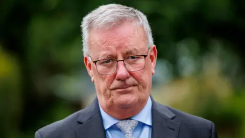 PA Media Mike Nesbitt, he is wearing a dark grey blazer with a blue shirt and a white and grey pattern tie. He has white hair and is wearing glasses.