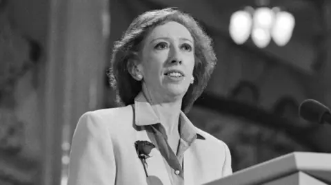 Steve Eason/Getty Images A black and white image of a woman standing at a lectern