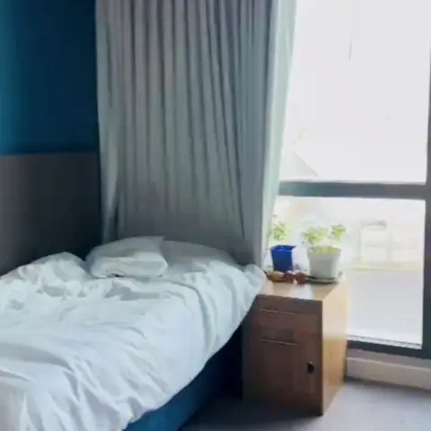 Inside of a hotel room showing a bed, table, and a window with a view outside.