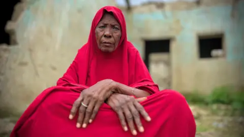 Gift Ufuoma / BBC Maryam Jidda sits as she wears a red jilbab and stares into the camera