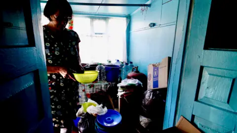 Darren Conway/BBC Olha stands in her home, filled with bottled water and rubbish