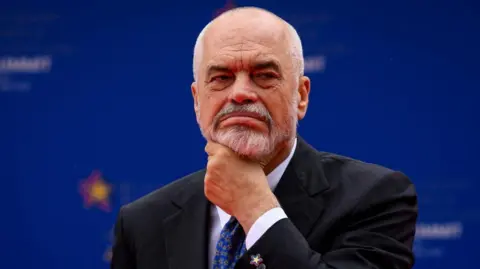 Reuters A man with a grey beard and moustache puts his hand on his chin and frowns