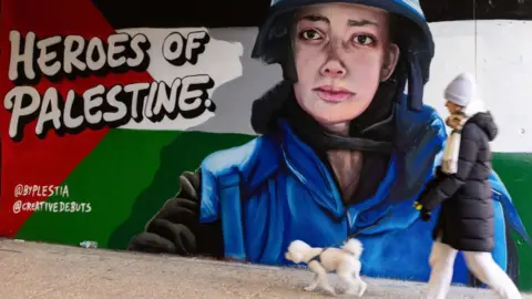 Getty Images A member of the public walks a dog past pro-Palestinian street art in tribute to Plestia Alaqad in an underpass. On the mural, there are the words 'Heroes of Palestine'. Plestia is wearing a blue press-jacket in the mural.