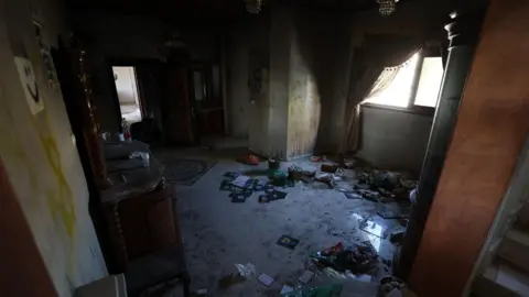 Interior image of an apartment shows graffiti on walls and burnt items and rubbish strewn on the floor.