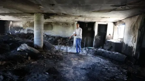 A man stands inside a burnt room.