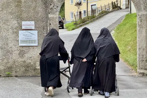 The three nuns walk away with their backs to the camera