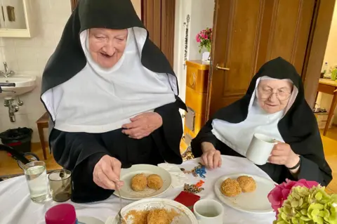 @nonnen_goldenstein Two nuns have food at dinner as one of them serves it