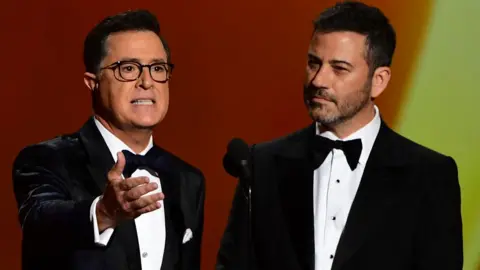 Getty Images Stephen Colbert (L) and Jimmy Kimmel, both wearing black tuxedos, speak onstage during the 71st Emmy Awards at the Microsoft Theatre in Los Angeles on September 22, 2019