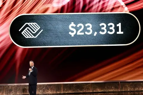 Getty Images Emmys host Nate Bargatze speaks onstage at the Emmy Awards with a large sign behind him saying $23,331 next to a logo for the Boys and Girls Club of North America. 