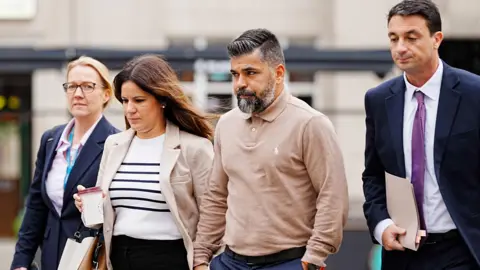 PA Media Alexandra and Sergio Aguiar walk hand-in-hand flanked on either side by their legal representatives, a woman and a man.