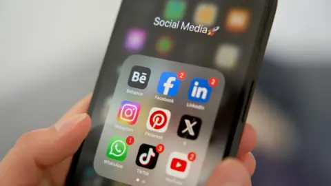 Getty Images A black phone with social media apps in a group on the screen.