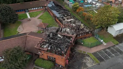 PA Media An aerial photo of the fire damaged office, the entire roof of the brick building has been destroyed with blackened beams visible.