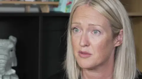 BBC Esther Ghey with long blonde hair and green eyes and gold nose ring sitting in a room with a black cabinet behind her.