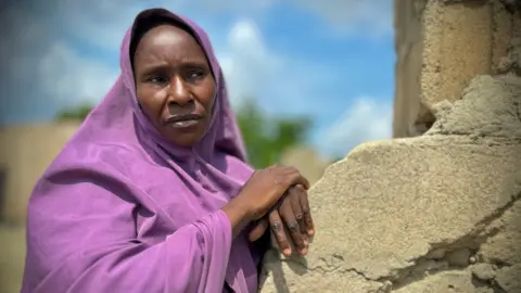 Gift Ufuoma / BBC Sa'adatu Dahiru leans on what appears to be the remains of a destroyed building whilst wearing a purple jilbab.