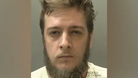 South Wales Police A custody image of a man with a beard and a whispy moustache