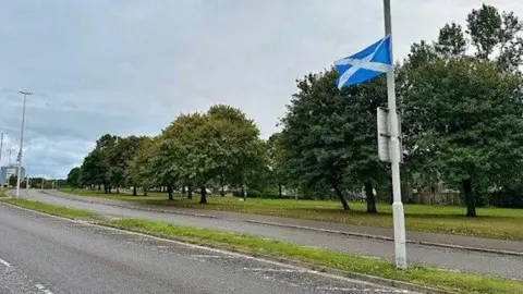 BBC A blue and white saltire flag is fluttering from a lamppost on an Aberdeen street, lined with trees.