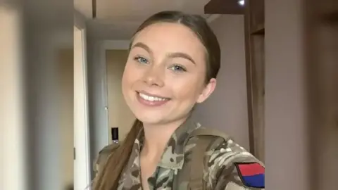 Family Handout Jaysley Beck smiles in a selfie, taken inside a room, wearing her Army uniform