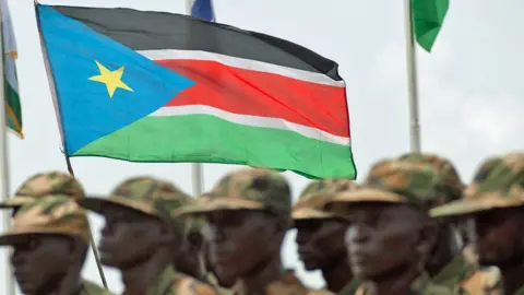 AFP/Getty Images A blurry image of South Sudanese soldiers parading with their national flag.