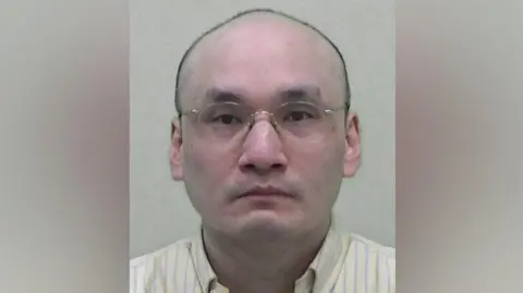 Northumbria Police Mugshot of Thomas Kwan. He is bald and clean shaven with thin framed glasses.