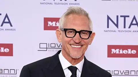 Getty Images Gary Lineker is smiling at the camera, dressed in a black suit with a white shirt and dark tie