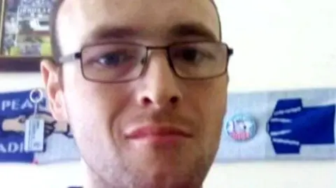 Police Scotland A man with short brown hair and glasses looks at the camera. He appears to be in a bedroom or living room