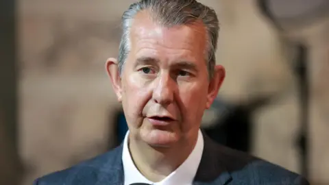 PA Wire Edwin Poots has short grey hair and is wearing a grey suit and white shirt. The background is blurred.
