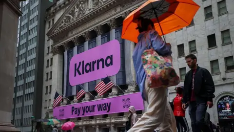 Bloomberg/Getty A fuschia sign saying Klarna, and Pay your way, drape the outside of the New York Stock Exchange, as people holding umbrellas walk by on the day of its debut on the New York Stock Exchange (NYSE) in New York, US, on Wednesday, Sept. 10, 2025.