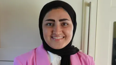 Salma Niazi Salma Niazi smiles at the camera. She is wearing a black head covering, a white shirt, and a pink blazer.